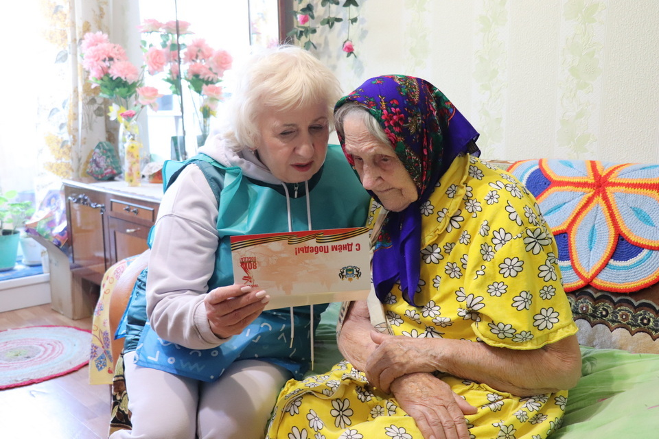 Горожанке Юлии Степановне Сердюковой (справа), которая в годы Великой Отечественной войны трудилась на колхозных полях, работала в детском доме и амбулатории в селе Бигила, поздравления от губернатора с Днём Победы вручает серебряный волонтёр Тамара Гилёва